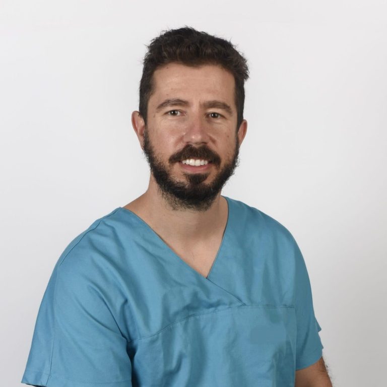 Hombre sonriente con barba, vestido con una camisa de consulta azul.