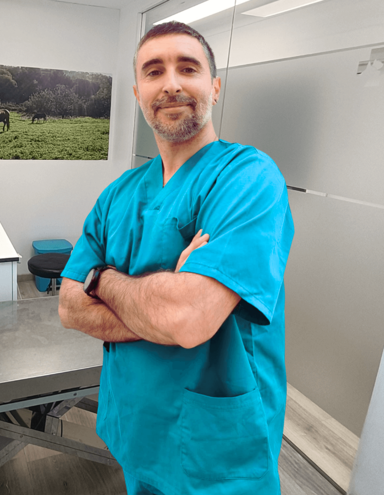 Hombre con bata azul en un entorno clínico, sonriendo y cruzando los brazos.